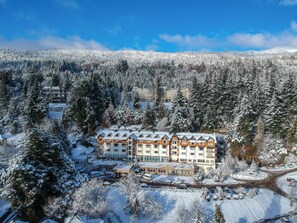 Ein mehrstöckiges Hotel inmitten dicht bewaldeter Landschaft, bedeckt von einer Schneedecke.
