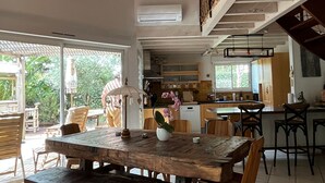 Een ruime eethoek met een houten tafel en stoelen, een hanglamp en uitzicht op de keuken en buitenruimte.