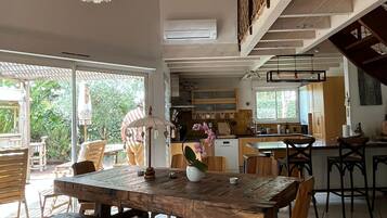 Un vaste espace de salle à manger avec une table et des chaises en bois, un luminaire suspendu et une vue sur la cuisine et l’espace extérieur.