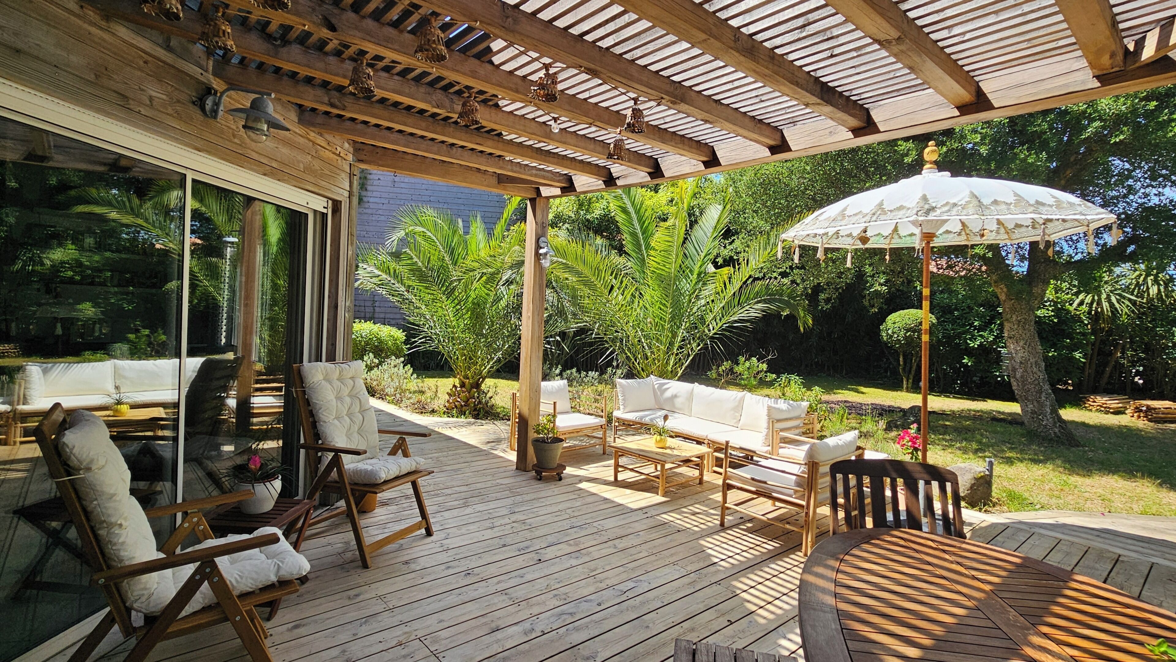 Une terrasse extérieure couverte, aménagée avec du mobilier en bois, notamment des chaises et une table, et dotée d’un grand parasol pour créer de l’ombre.