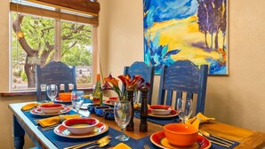 Uma mesa de jantar posta com pratos coloridos, copos e um vaso com flores.