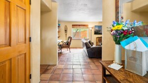 Um corredor com porta de madeira, área de jantar com mesa e cadeiras, um sofá e um vaso com flores.