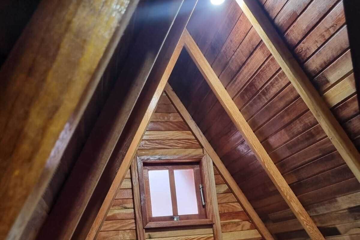 A cozy attic bedroom with a wooden sloped ceiling, a small window, and a bed with green pillows.