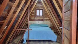 Quarto de sótão com teto inclinado de madeira, uma cama de solteiro e uma janela.