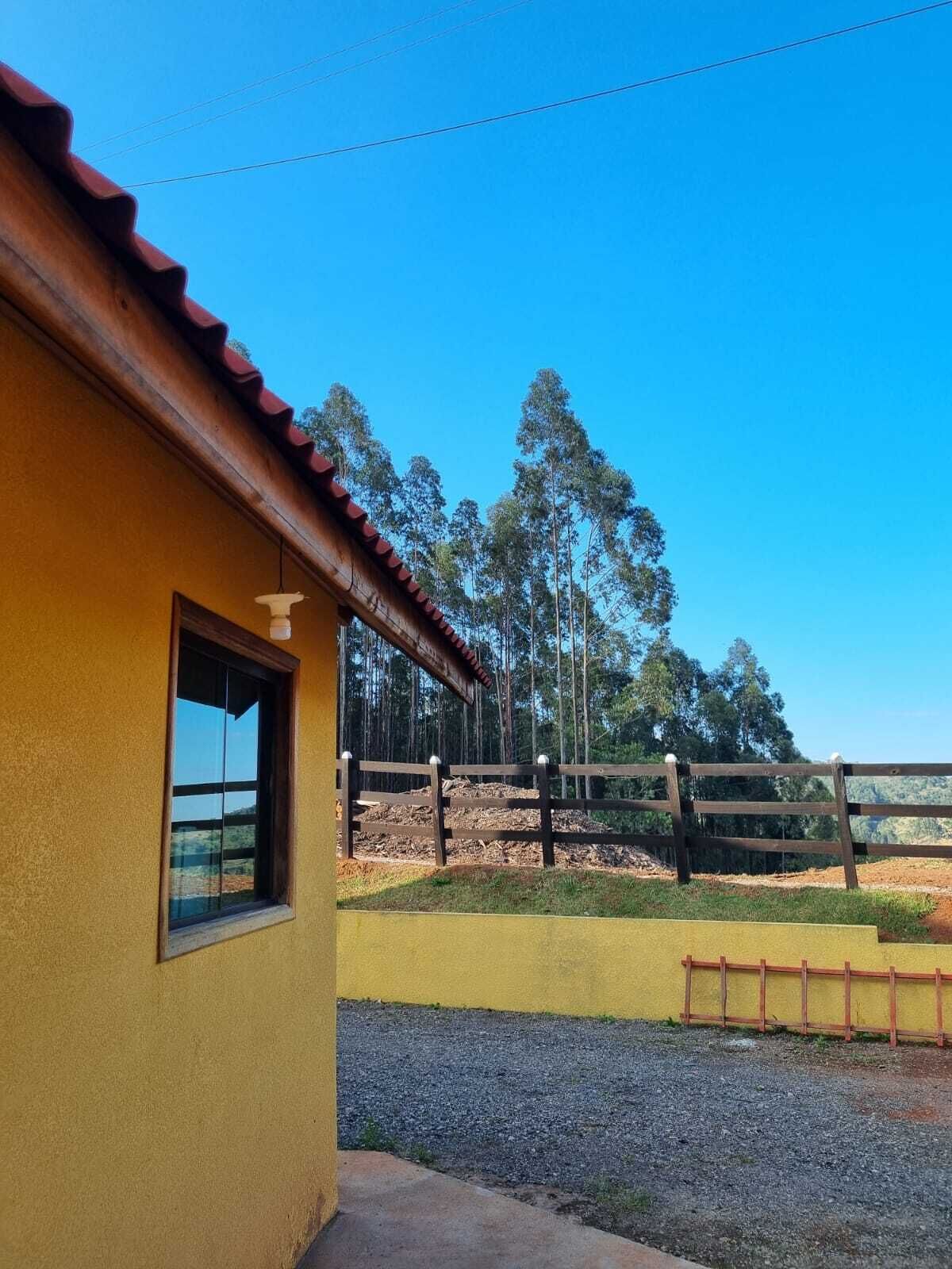 A yellow building with a red roof, a window, and a gravel path leading to a wooden fence.