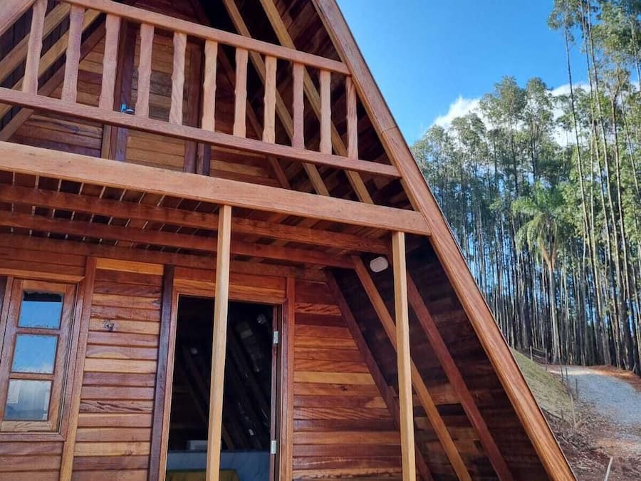 Una cabaña de madera con techo triangular, un balcón y una puerta que da a un espacio interior.