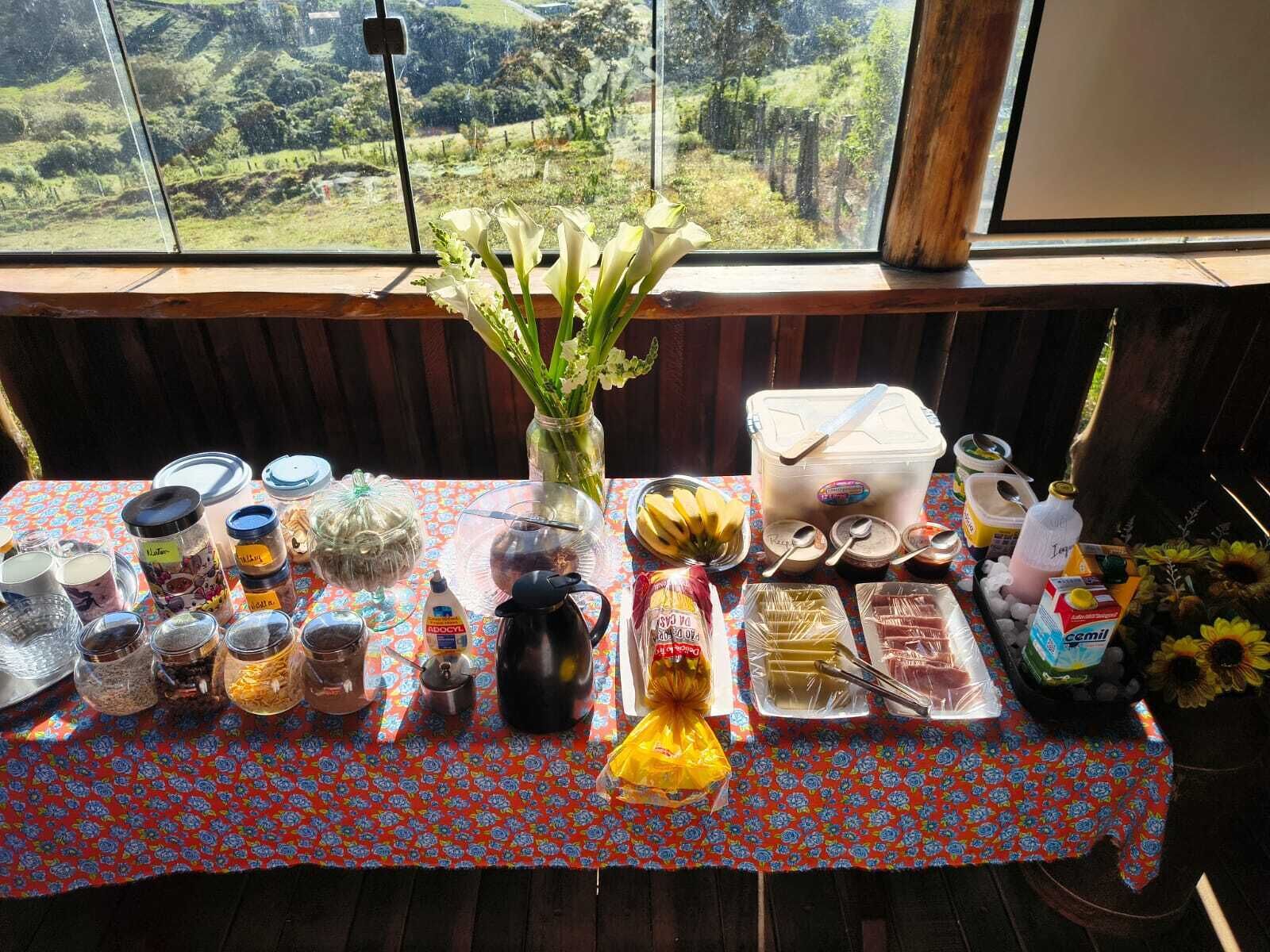 Una mesa con alimentos y un florero, frente a una ventana con vistas a un paisaje verde.