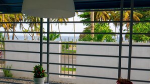Una habitación con vistas a palmeras y al océano a través de una ventana con persianas horizontales.