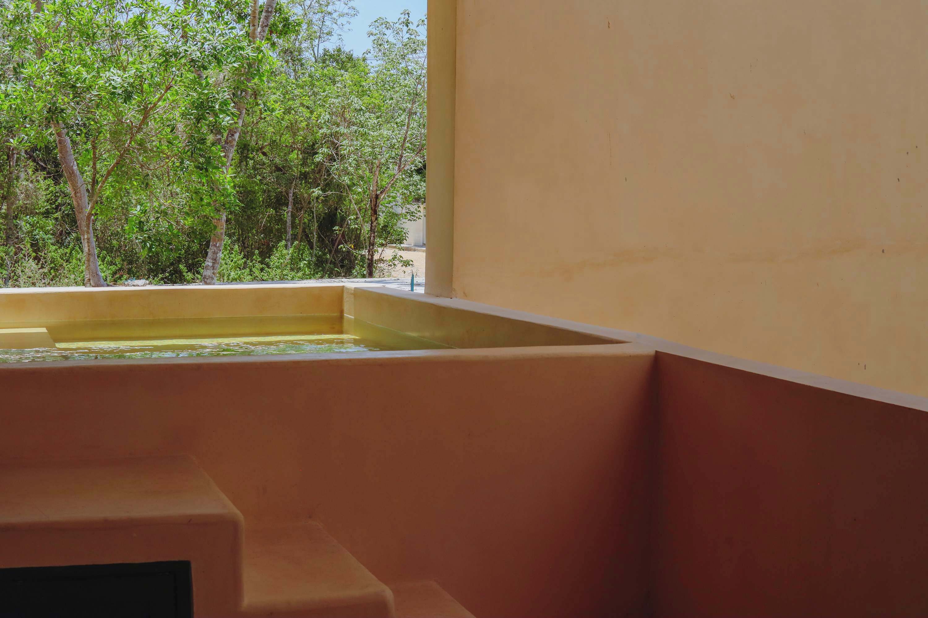 Habitación con ventana que da a un jardín, una piscina pequeña y una pared sencilla.