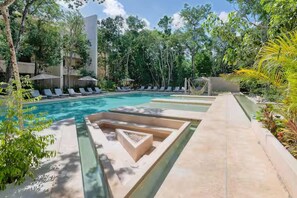 Un área de piscina con sillones de descanso, una piscina cristalina y follaje circundante.