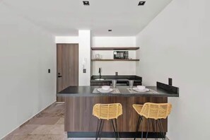 Una cocina moderna con una isla central, dos taburetes de bar y un microondas en un estante.