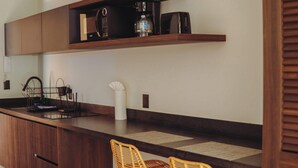 A kitchen with wooden cabinets, a coffee machine, and wicker chairs. - Chic Jungle 1BR: Balcony Priv Pool, Steam & Gym (Tulum)