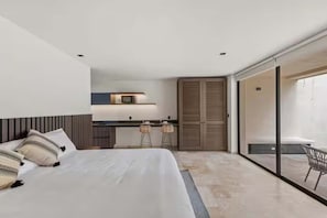 Een moderne slaapkamer met een bed, een kleine kitchenette en een schuifdeur naar een buitenruimte.