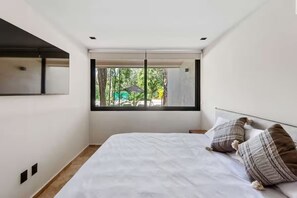 Een slaapkamer met een bed, een raam en uitzicht op groen.