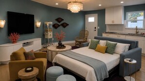 Ein modernes Schlafzimmer mit Bett, Sofa, Hocker, Fernseher und Essbereich.