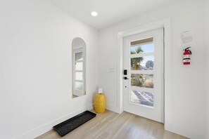 A hallway with a white door, a yellow vase, a black mat, and a fire extinguisher on the wall. - Steps to Beach + Private Pool, Theater & Arcade (St. Augustine)