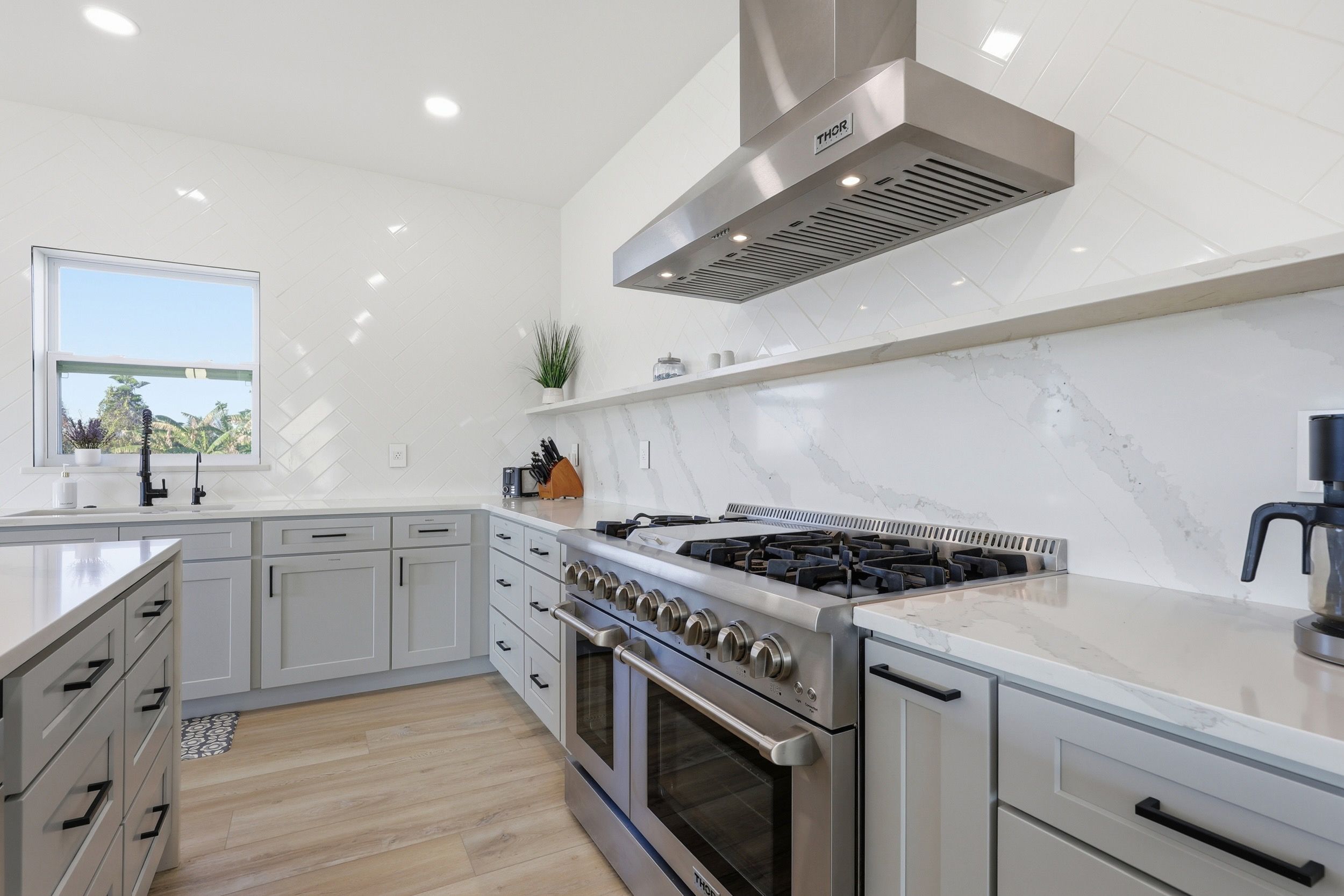 A modern kitchen with a stainless steel range hood, a built-in oven, and a marble backsplash.