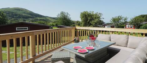 An outdoor deck with a wicker sofa, a table with glasses and watermelon slices, and a wooden railing.