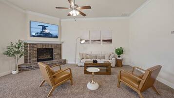 A living room with a fireplace, two brown leather chairs, a white coffee table, a ceiling fan, and a TV mounted on the wall.