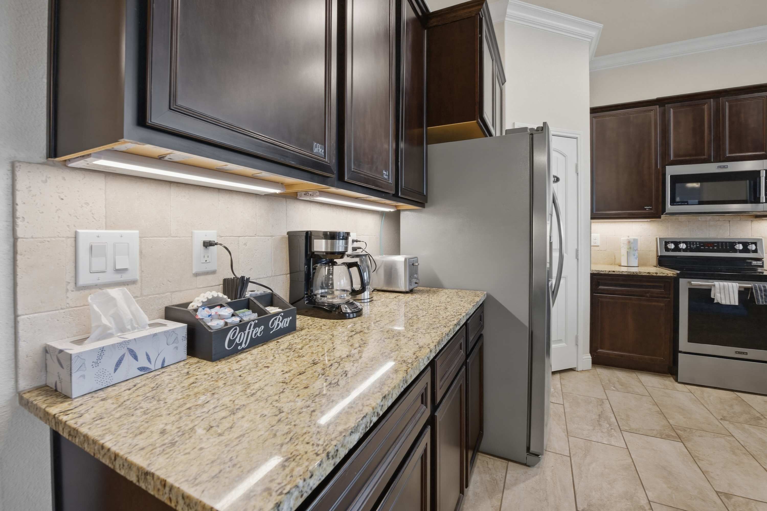 A kitchen with dark wood cabinets, a stainless steel refrigerator, a microwave, and a coffee maker.