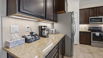 A kitchen with dark wood cabinets, a stainless steel refrigerator, a microwave, and a coffee maker.