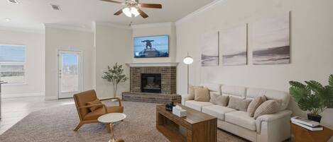 A spacious living room with a fireplace, a ceiling fan, a television, and a large window.