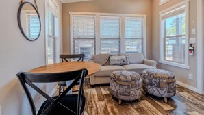 A room with a wooden dining table, a sofa, and ottomans.