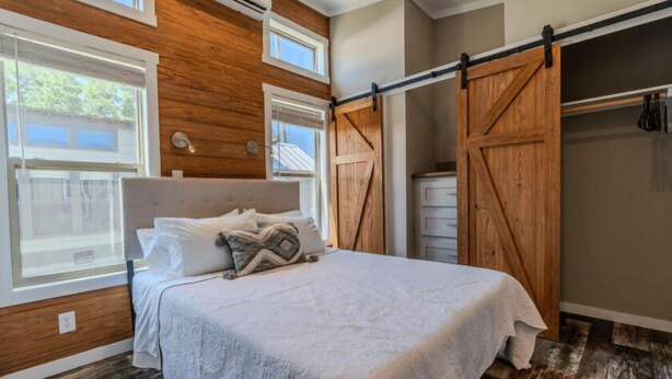 A bedroom with a bed, wooden walls, a closet with a sliding door, and a window.