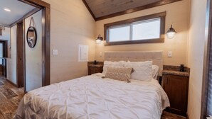 A bedroom with a large bed, a headboard, two bedside tables, a window, and a door.