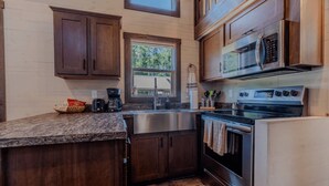 A compact kitchen with dark wooden cabinets, a stainless steel sink, a built-in microwave, and a stove.