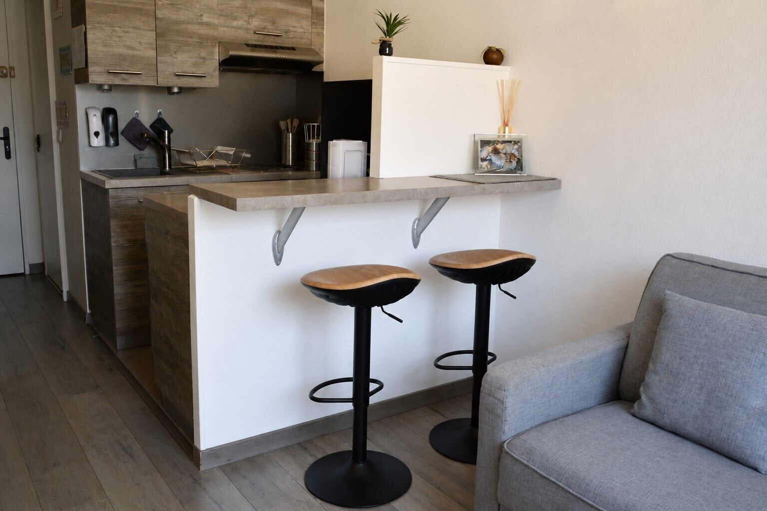 Eine moderne Küche mit Holzausbau, einer integrierten Kochinsel mit Barhocker und einem grauen Sofa.