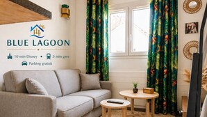 A cozy room with a sofa, a small round table, and a decorative wall with a logo and amenities information. - Blue Lagoon | Cozy Duplex • Parking • Disneyland, 10 min (Bussy-Saint-Georges)