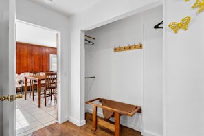 Un pasillo con un perchero, un banco y un comedor con sillas y una mesa.