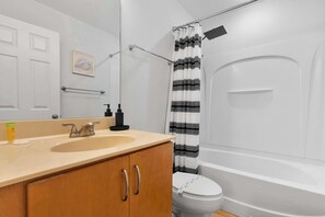 Et badeværelse med vask, spejl, toilet og bruseforhæng.