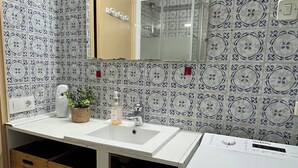 Une salle de bain avec des carreaux décorés, un meuble-lavabo à deux vasques, des tiroirs de rangement en bois et un miroir avec un éclairage au-dessus.