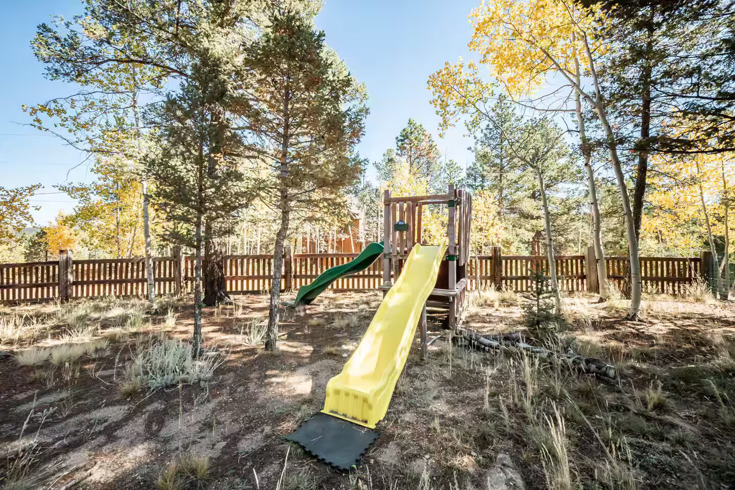 A playground with a slide and climbing structure surrounded by trees.