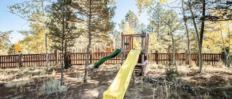 Un parque infantil con un tobogán y una estructura para escalar rodeado de árboles.