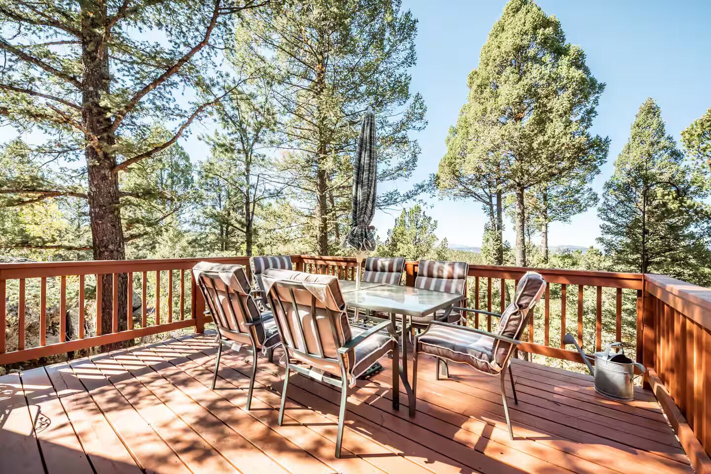 A wooden deck with a table and chairs, surrounded by trees.