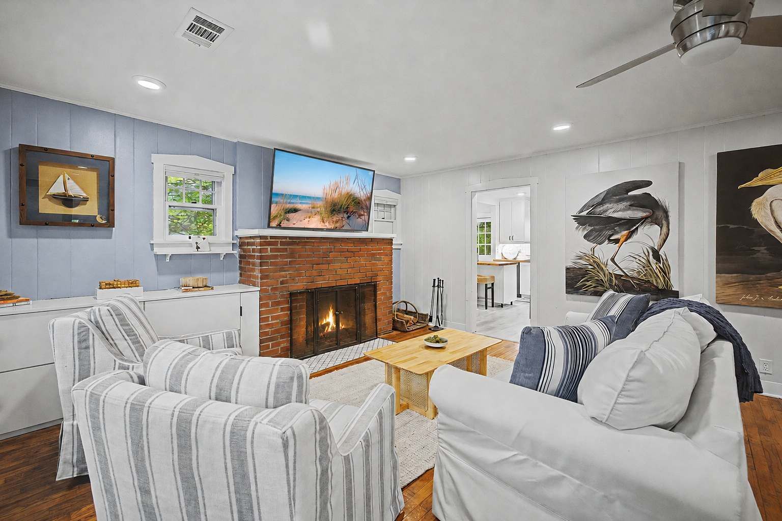 A living room with a fireplace, striped chairs, a television, and artwork on the walls.