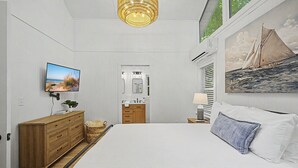 Un dormitorio con cama, televisión, un cuadro, cómoda y ventana.