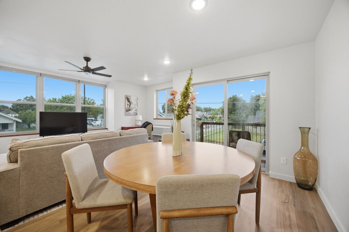 A modern living room with a sofa set, a round dining table, and a large window with a view of the outdoors.