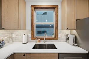 Una cocina con ventana, encimera blanca, armarios de madera y lavavajillas integrado.