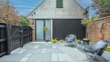 Une maison avec un toit gris, une porte noire et une porte de garage noire. Il y a un petit jardin avec une plante en pot et une chaise.
