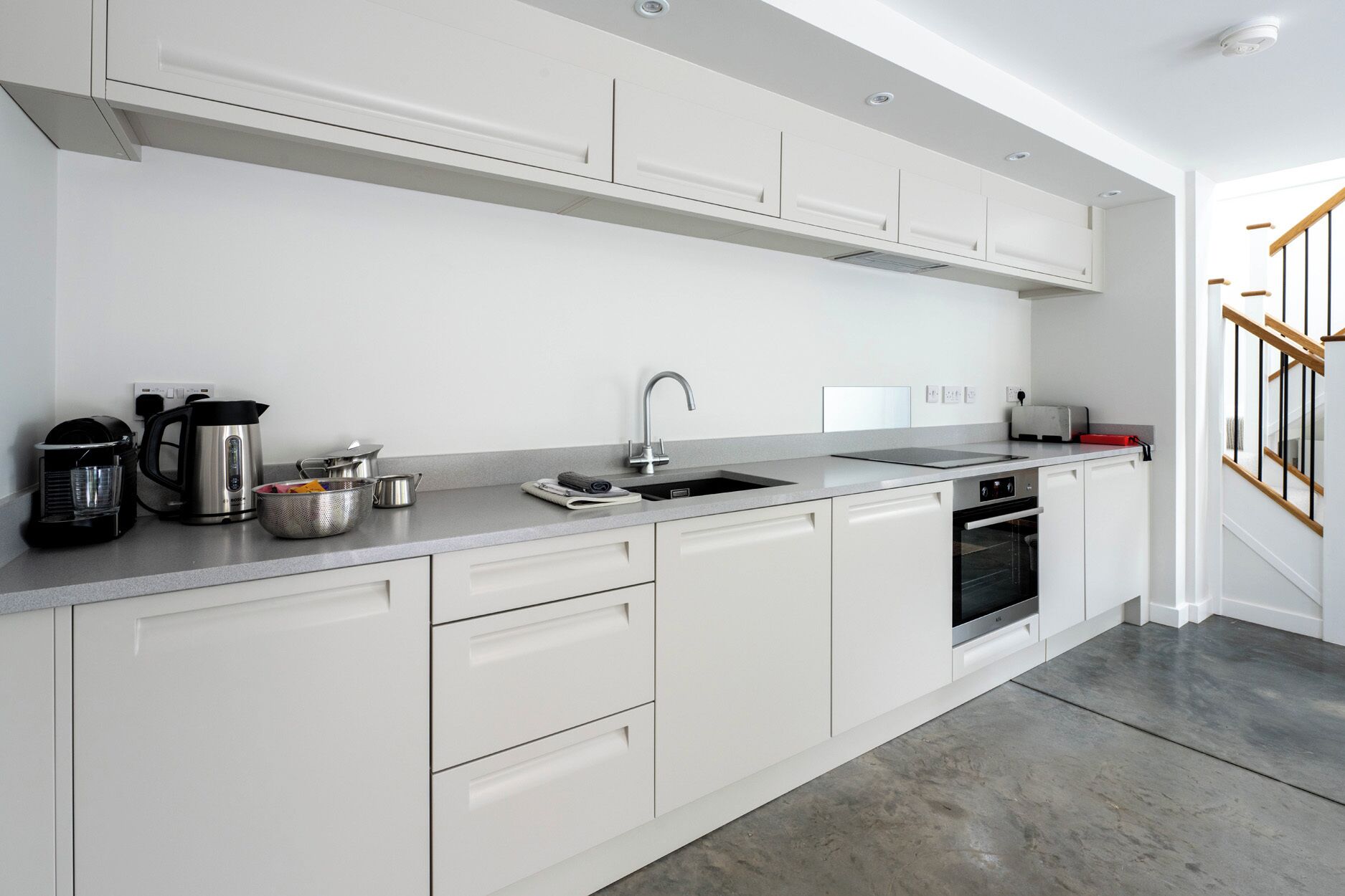 A modern kitchen with white cabinets, a stainless steel sink, a kettle, a toaster, and an oven.
