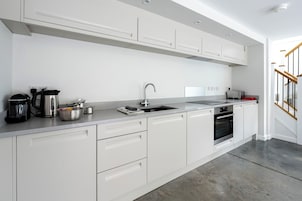 Una cocina moderna con armarios blancos, un lavamanos de acero inoxidable, una tetera, un tostador y un horno.
