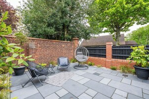 Un patio con pared de ladrillo, una silla colgante, una silla de metal y plantas en macetas.