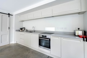 Una cocina moderna con armarios blancos, un horno de acero inoxidable, un lavamanos y un tostador.