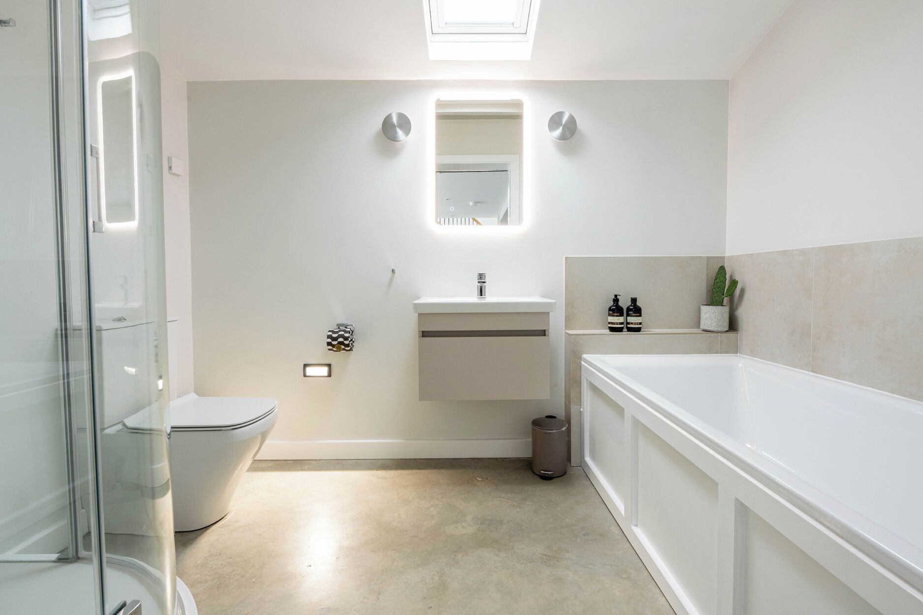 A modern bathroom with a glass shower enclosure, a white toilet, a sink with a mirror, a bathtub, and a trash can.