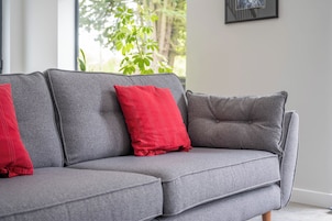 Un sofá seccional gris con cojines rojos en una habitación con ventana y un cuadro en la pared.