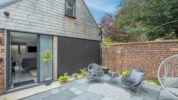 Une maison moderne dotée d’une grande porte-fenêtre coulissante qui donne sur un espace de vie, d’un mur en briques et d’une terrasse avec des meubles d’extérieur.